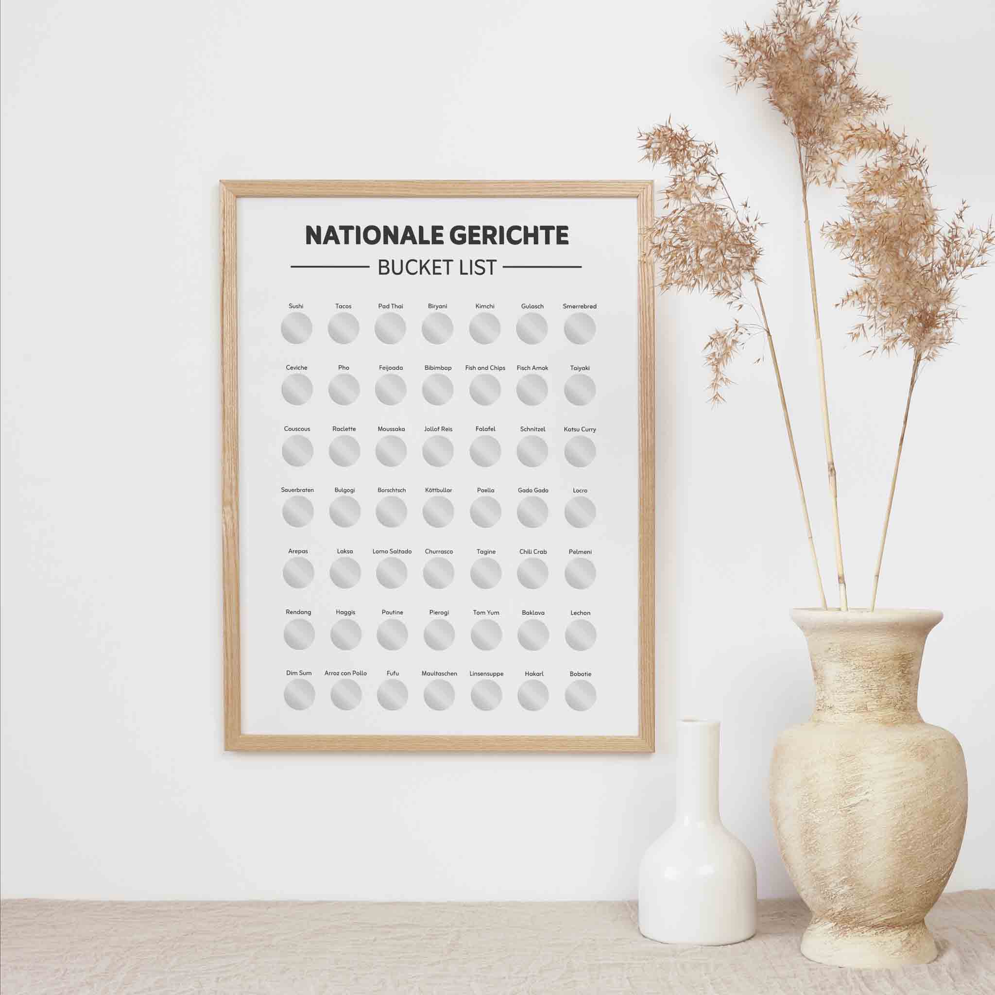 The Bucketlist Nationale Gerichte Rubbelposter A3 von funkenschauer hängt gerahmt an einer weißen Wand, neben beigem Pampasgras in einer Tonvase und einer kleinen weißen Vase - das perfekte Geschenk für Foodies und Kulinarik-Fans.