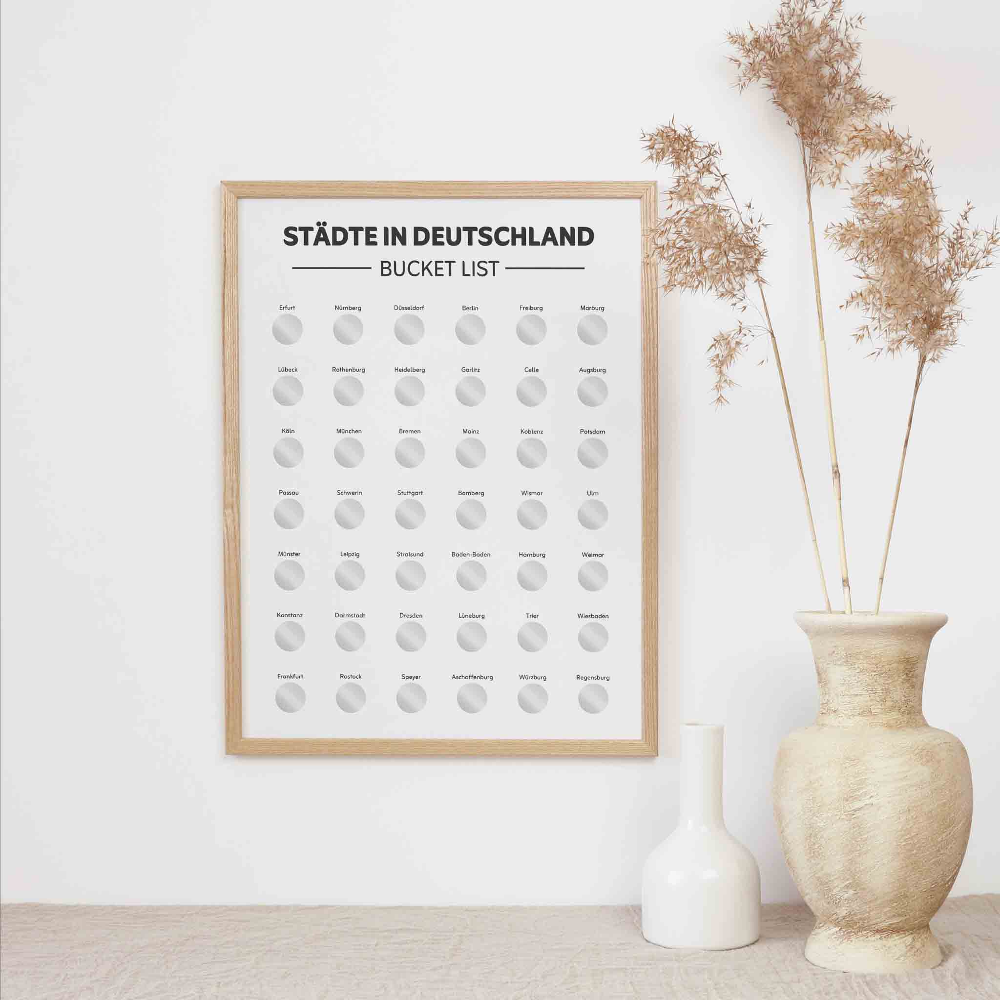 Das funkenschauer Städte Deutschland Bucketlist zum Freirubbeln A3 Poster hängt an einer weißen Wand neben beigem Pampasgras und zwei Vasen. Mit Rubbelfeldern für deutsche Städte, ist es ein perfektes Reisegeschenk für Abenteuer und Weihnachten.