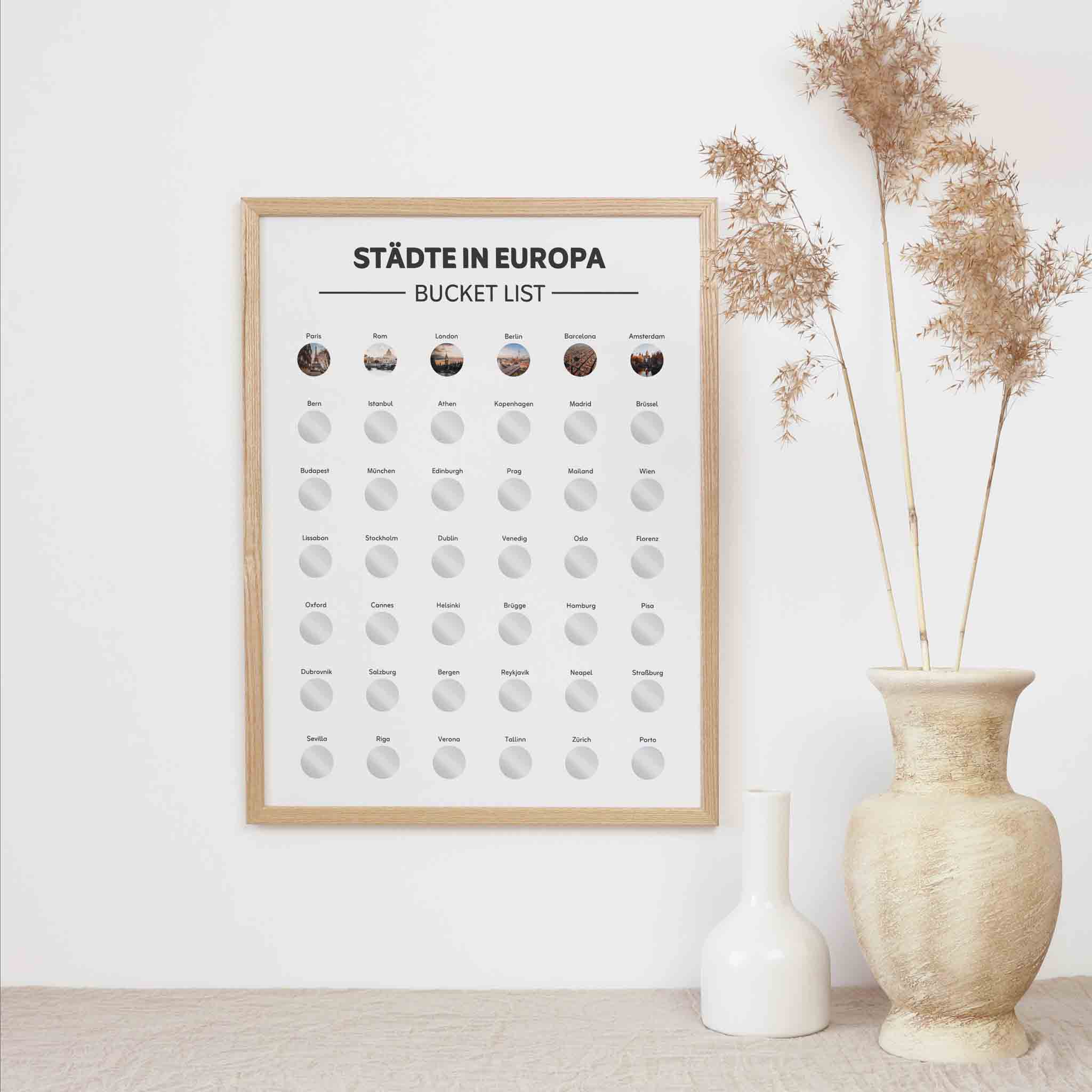 Das funkenschauer Poster Europa A3 - Rubbelkarte mit Städten wird an einer weißen Wand mit einer beigen Vase mit getrocknetem Gras und einer kleinen weißen Keramikflasche gezeigt. Diese Rubbelkarte ist ein ideales Reisegeschenk und Löffelliste-Inspiration.