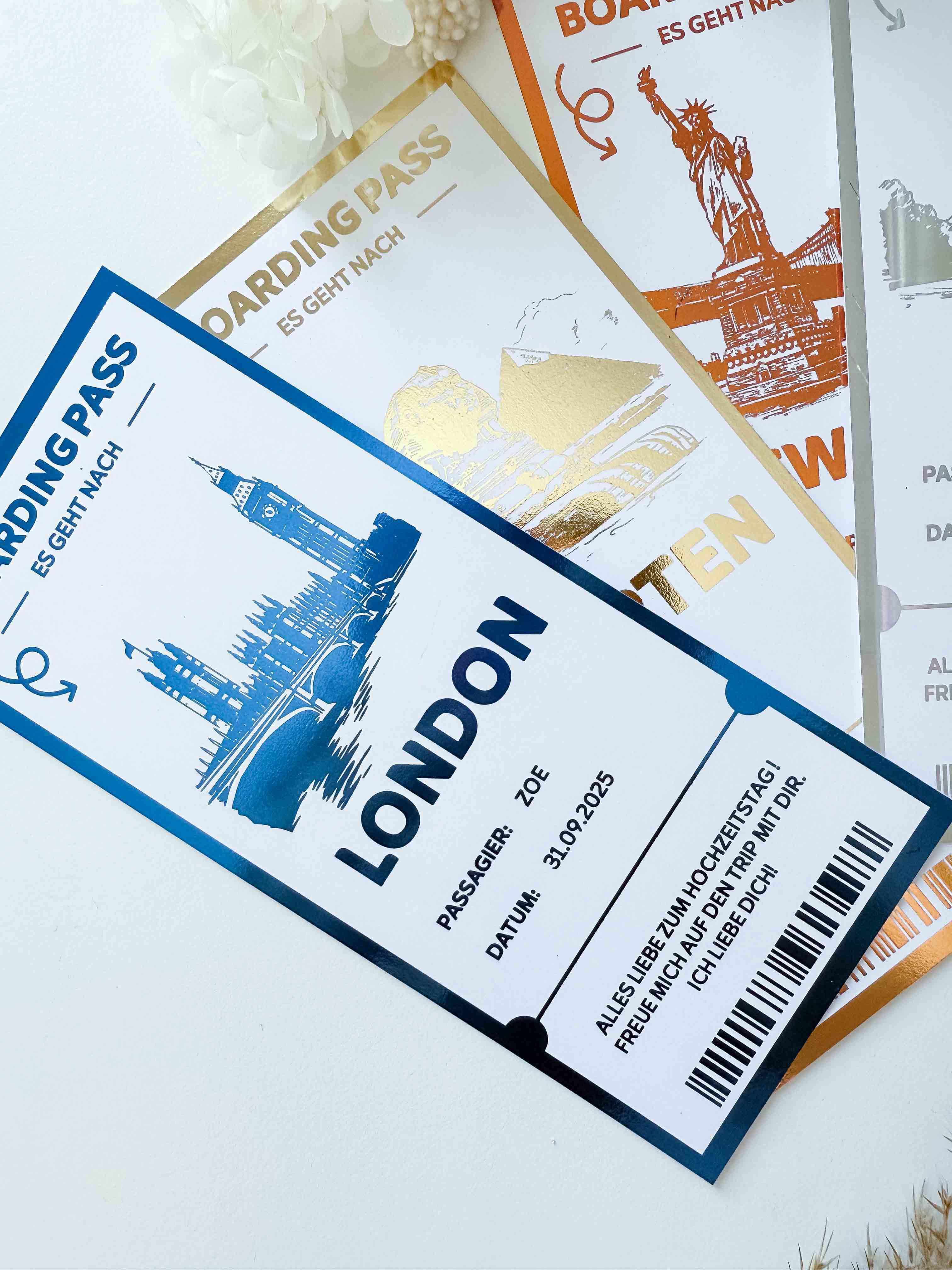 Drei personalisierte Reisegutscheine von funkenschauer mit jeweils einzigartigen Bordkartendesigns - einer mit der Aufschrift "London" mit blauen Akzenten und Wahrzeichen sowie goldene und silberne Versionen - sind die perfekte Inspiration für Reisegeschenke.