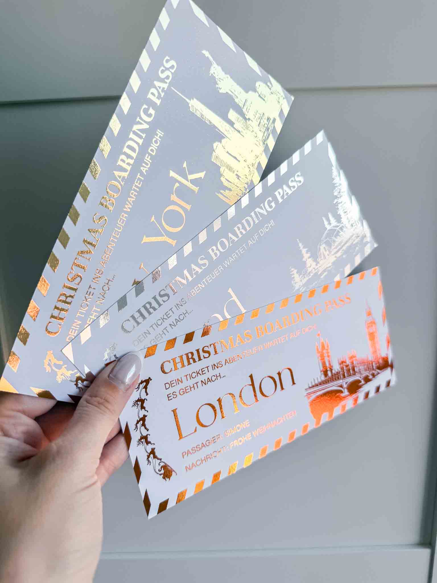 Eine Hand hält drei funkenschauer Reisegutscheine - personalisierte Weihnachtsgutscheine in Gold und Silber, jeweils mit festlichen Stadtmotiven für York, Edinburgh und London - perfekt als Weihnachtsgeschenk oder Reisegutschein.