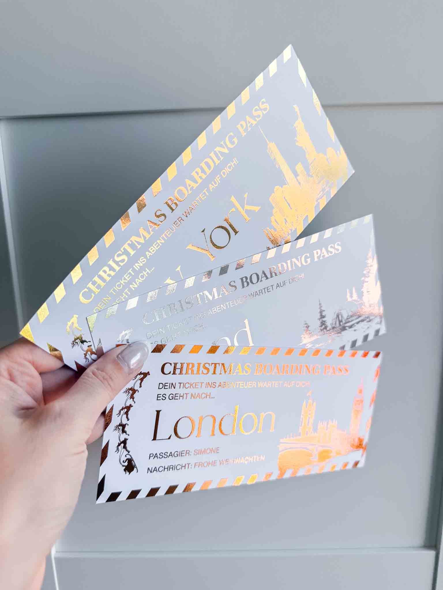 Eine Hand hält drei festliche funkenschauer "Reisegutschein Weihnachtsgutschein personalisiert" Tickets in Gold, Silber und Bronze-einzigartige Geschenke mit Zielen wie York und London, ideal als Gutschein Reise oder Weihnachtsgeschenk.
