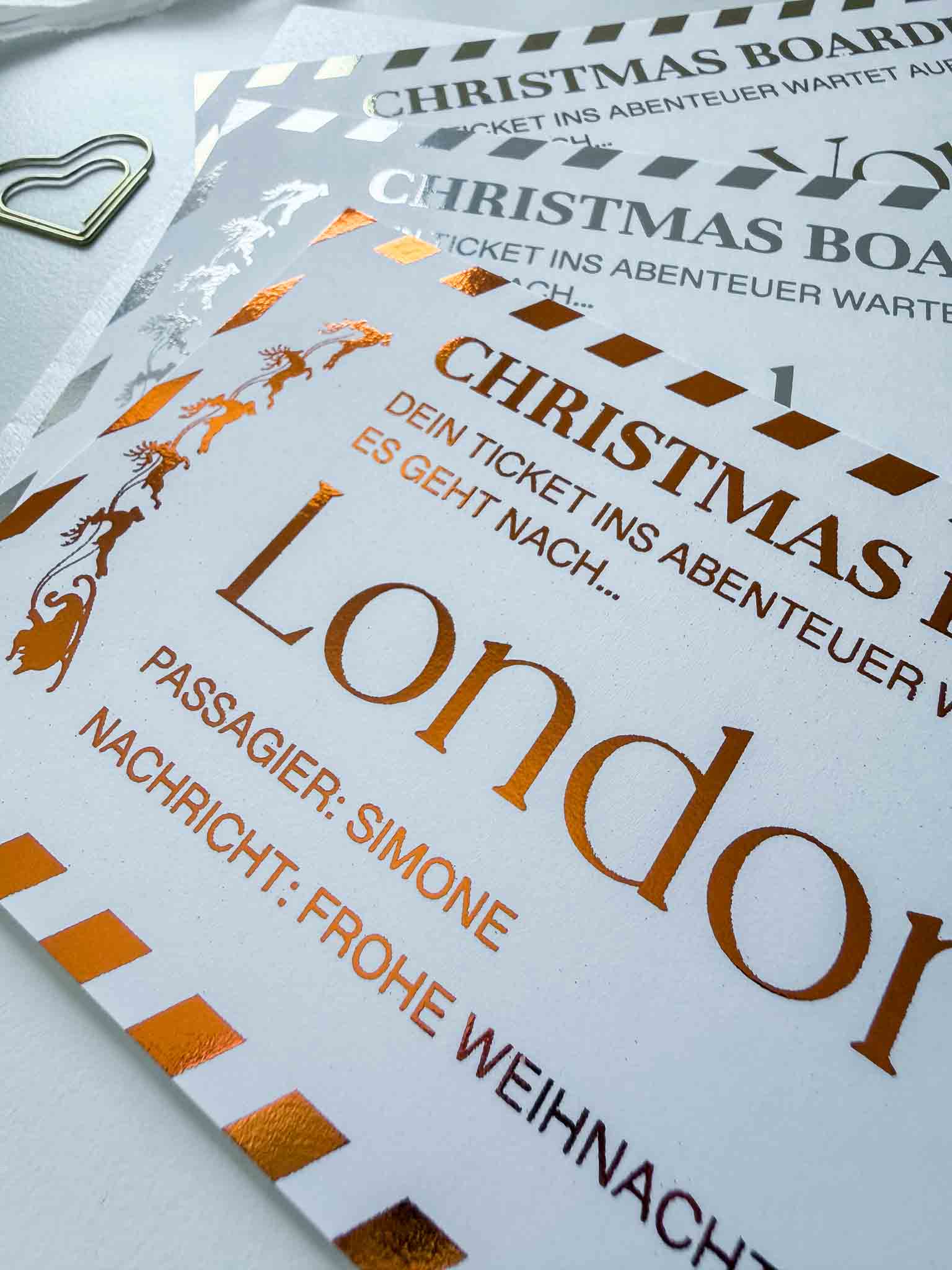 Eine Nahaufnahme eines personalisierten "Reisegutscheins Weihnachtsgutschein" von funkenschauer als Weihnachtskarte mit glänzendem Golddruck, Reise-Ticket nach London, Name "Simone" & Gruß: "Frohe Weihnachten" - perfekt als Geschenk oder Gutschein.