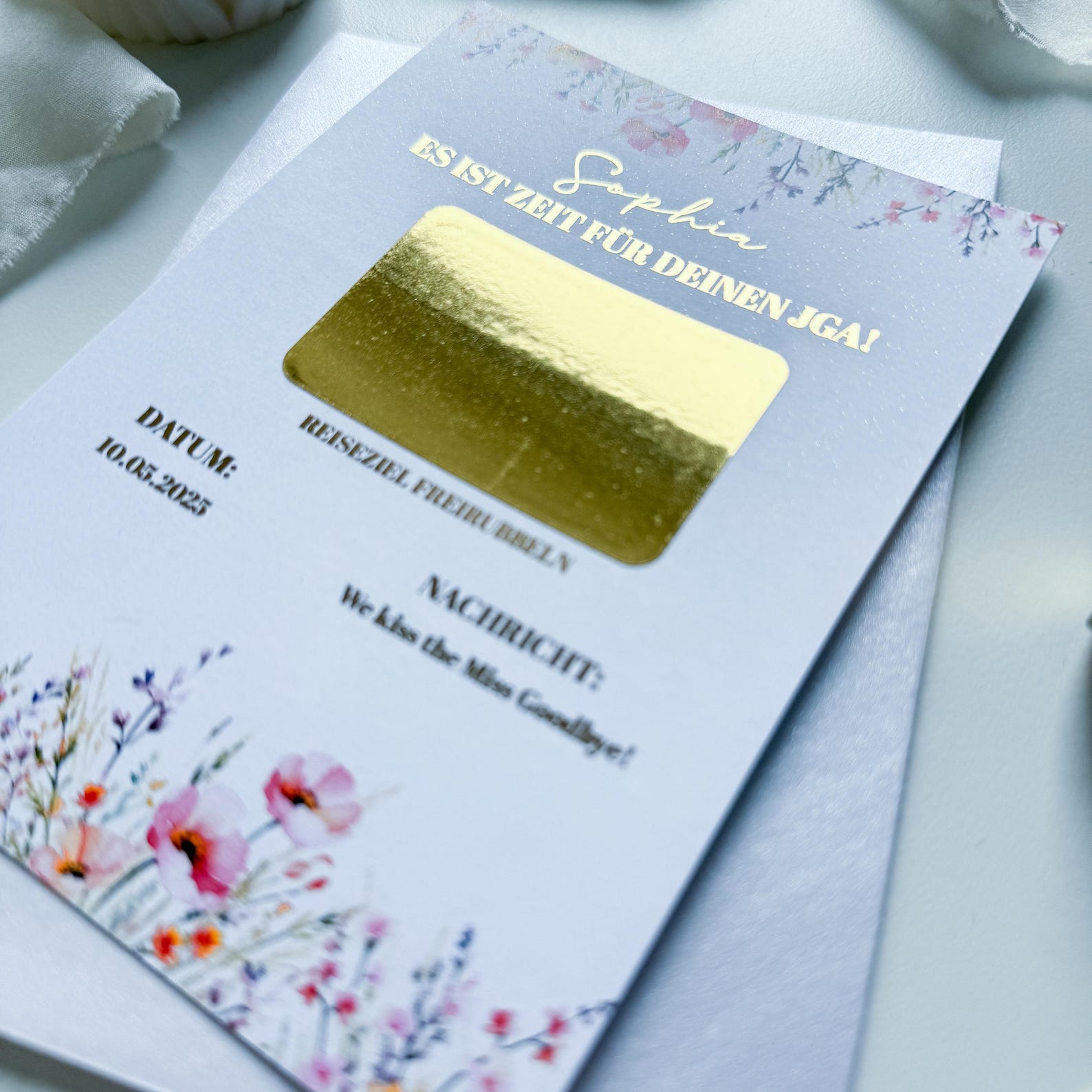Die A6-Rubbelkarte „JGA Gutschein – Wiesenglück“ von Funkenschauer besticht durch florales Design, goldene Folienakzente und pink-lila Blumen. Perfekt als Einladung zum JGA oder Wochenendtrip-Gutschein mit Platz für persönliche Angaben.