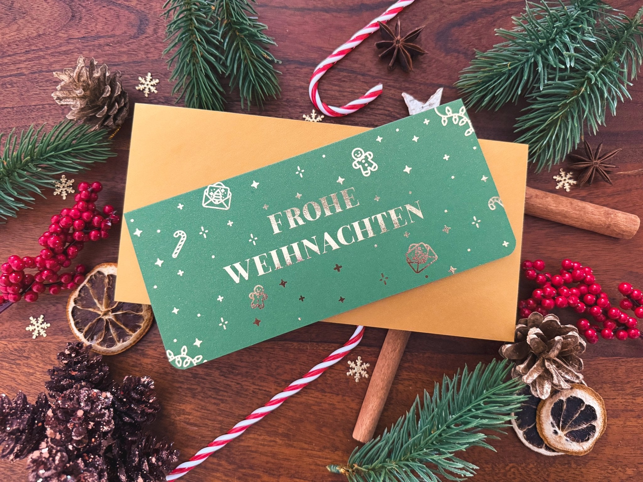Eine grüne Funkenschauer-Karte mit "Frohe Weihnachten" ruht auf einem goldenen Umschlag, der mit festlichen Akzenten verziert ist. Diese personalisierte Rubbelkarte ist das außergewöhnliche Weihnachtsgeschenk für gemeinsame Zeit statt Zeug - perfekt als Gutschein-Idee!.