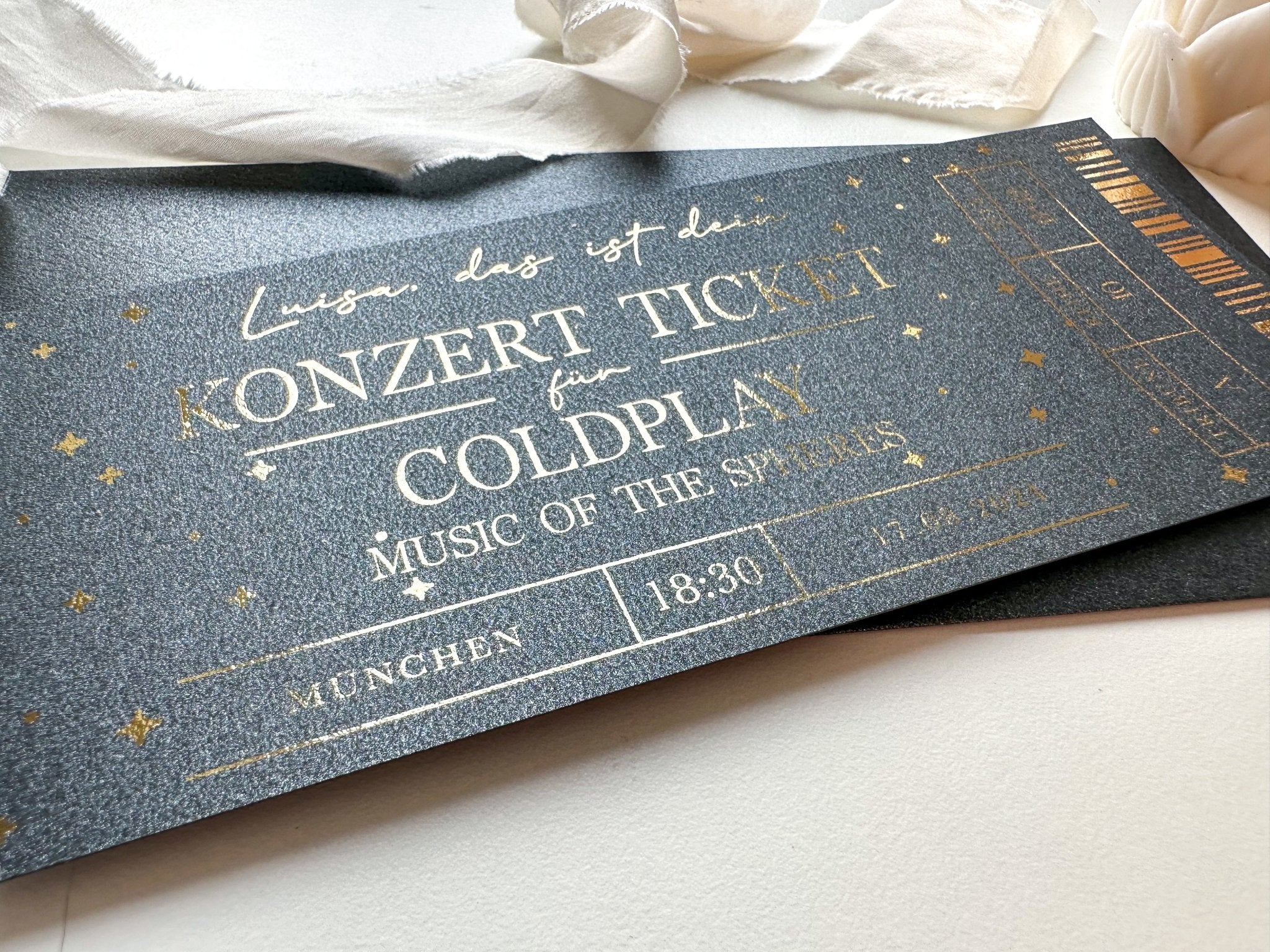 Ein glitzerndes schwarzes Konzertkarten-Geschenk von Funkenschauer mit goldenem Text und Sternen, personalisiert für Coldplays „Music of the Spheres“-Tour in München um 18:30 Uhr – eine ideale Geschenkidee für Musikliebhaber.