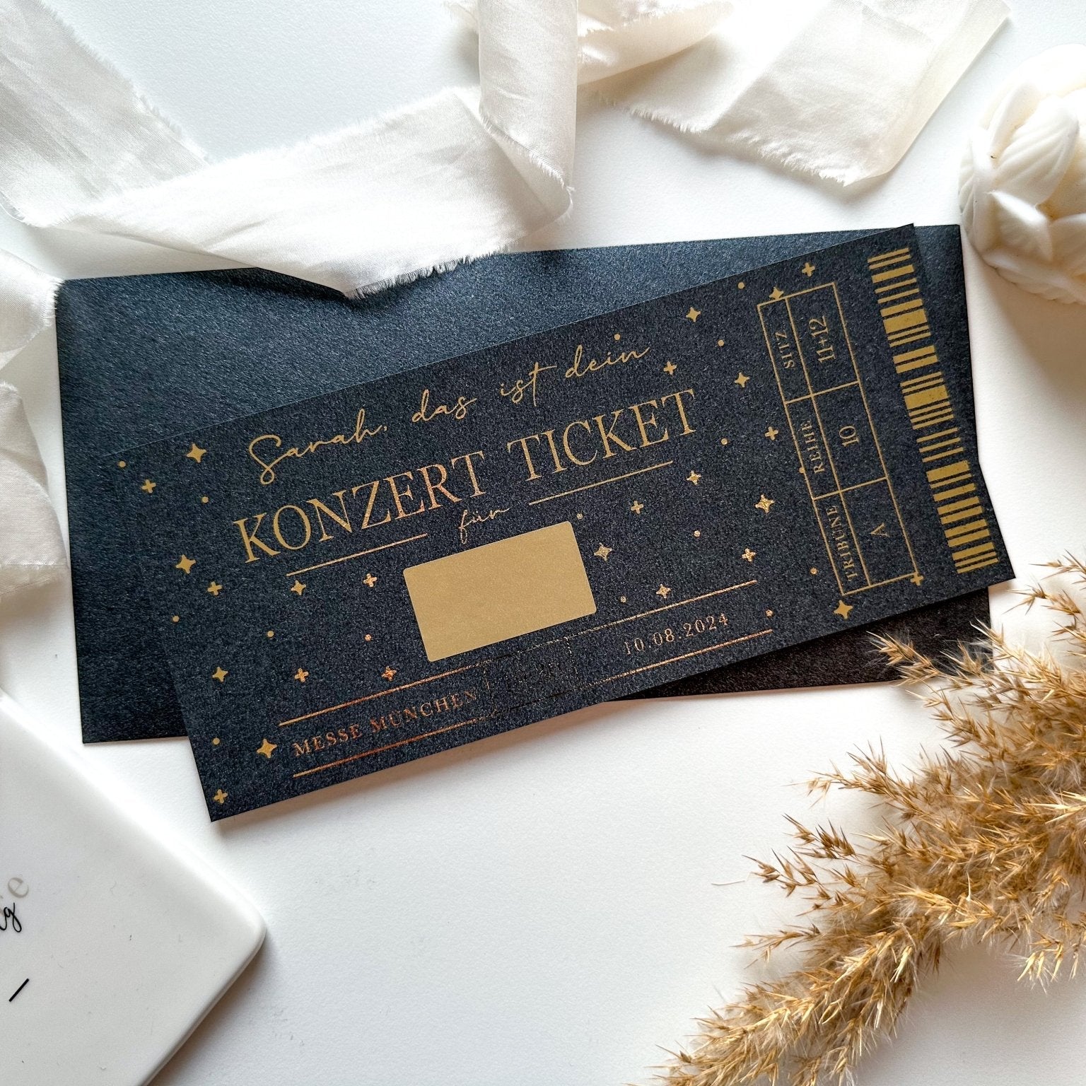 Ein schwarz-goldenes personalisiertes Gutschein Konzertticket von Funkenschauer mit Rubbelfeld und „KONZERT TICKET“ liegt auf weißem Untergrund mit Deko – das perfekte Geschenk für Musikliebhaber, als Rubbelkarte individuell gestaltbar.