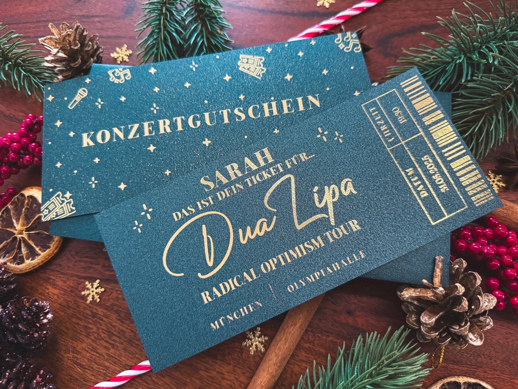 Ein funkenschauer Konzertgutschein Personalisiert für Dua Lipa, Coldplay oder Ed Sheeran liegt auf einem festlich dekorierten Holztisch - die perfekte personalisierte Konzertkarte als Weihnachtsgeschenk.