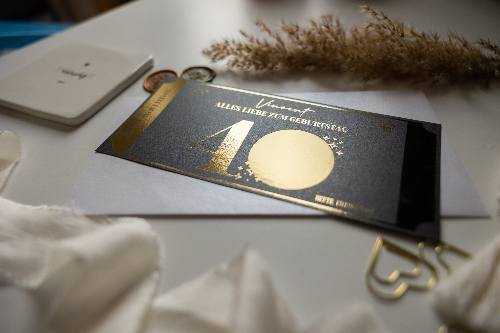 Auf einem Tisch steht auf Funkenschauers „Personalisierter Geburtstagsgutschein mit Rubbelfeld – Runder Geburtstag Geschenkidee“ „Alles Liebe zum Geburtstag“ mit einer großen goldenen „40“, die das Edles-Design zeigt, elegant umrahmt von Münzen, Pampasgras, einem weißen Tuch und einer kleinen weißen Karte.