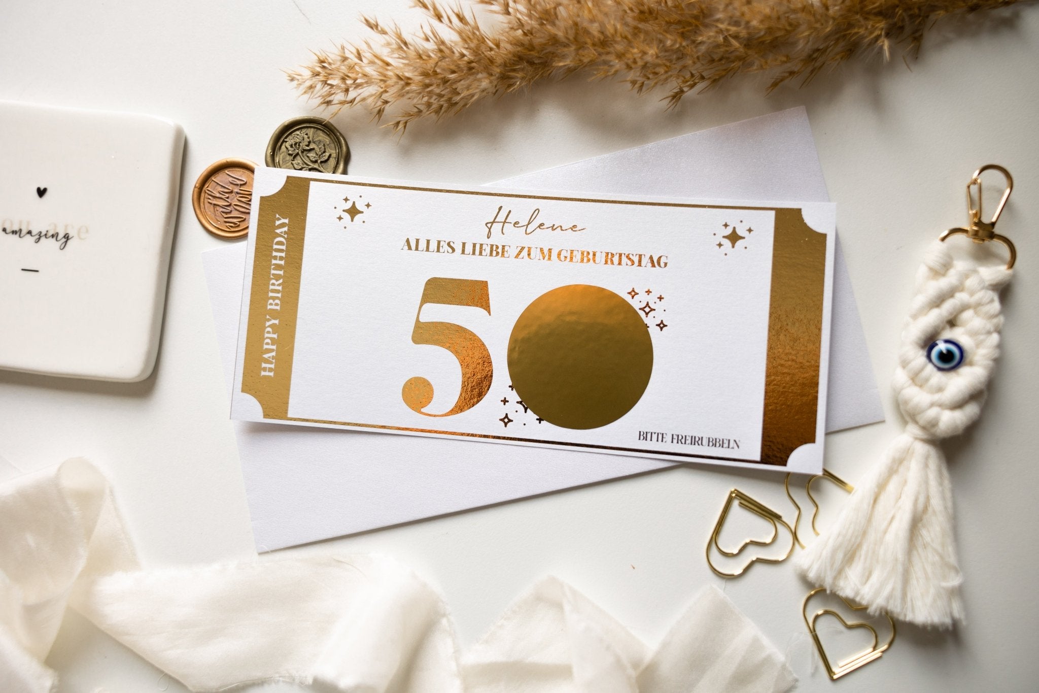 Der funkenschauer Geburtstagsgutschein enthält ein gold-weißes „50th“ mit „Alles Liebe zum Geburtstag“ und „Happy Birthday“, einen personalisierbaren Blankokreis, getrocknetes Pampasgras-Dekor sowie einen Quasten-Schlüsselanhänger und eine herzförmige Büroklammer, alles im edles-Design.