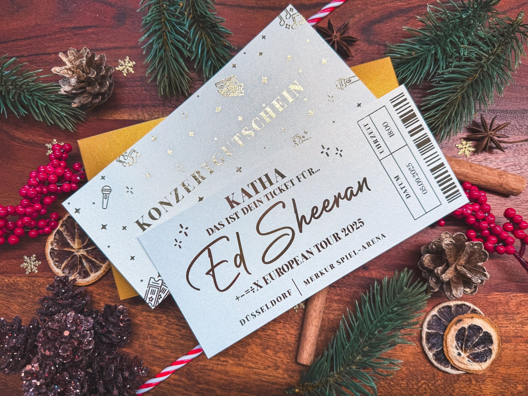 Eine Nahaufnahme des personalisierten Konzertgutscheins von funkenschauer fängt das Feiertagsthema ein und zeigt kreative Konzertkarten mit einem luxuriösen Ticketdesign auf einer festlichen Holzoberfläche, die mit Tannenzweigen, roten Beeren, goldenen Sternen, getrockneten Orangenscheiben und einem Zuckerstangen verziert ist.