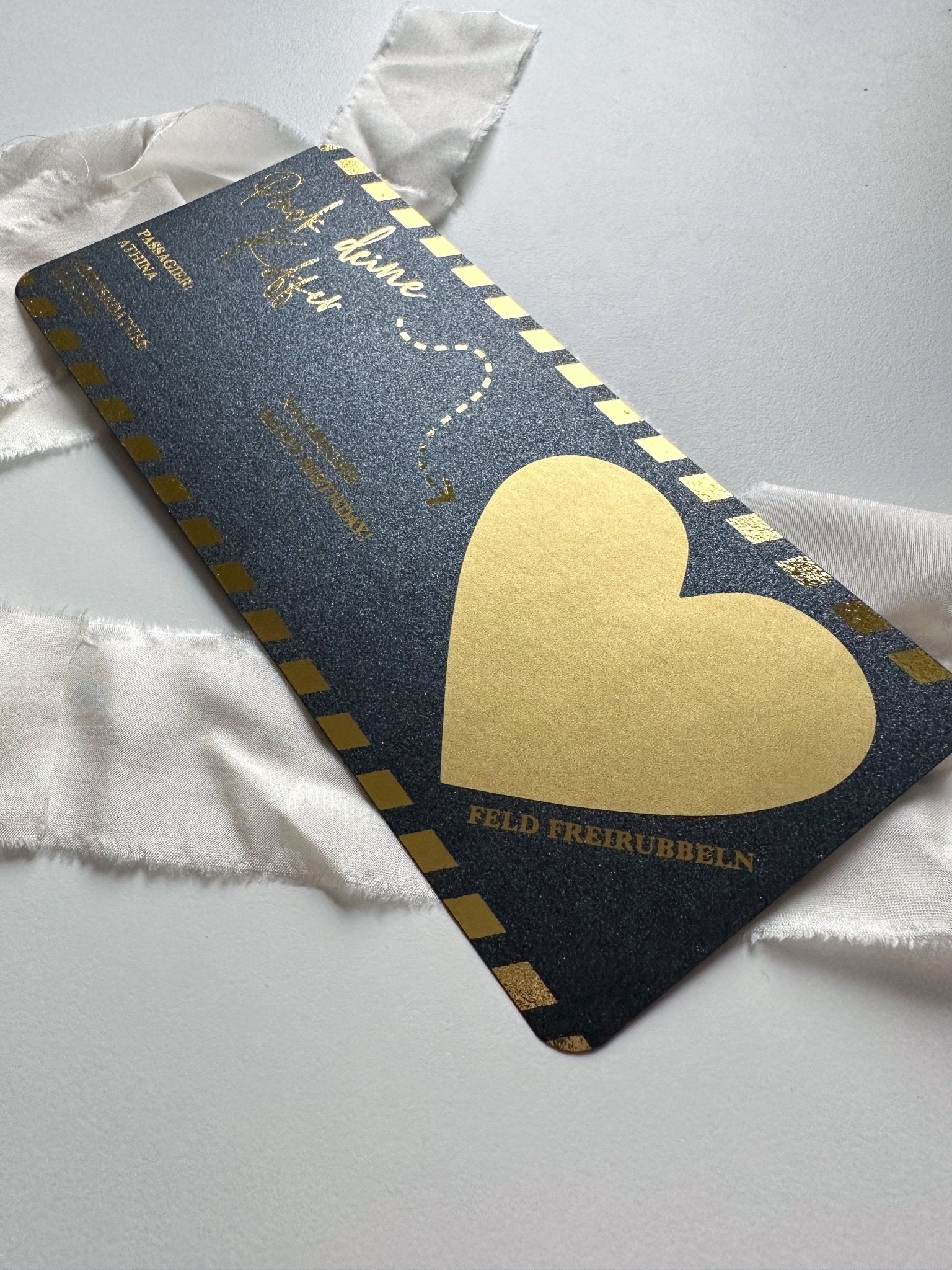 Der funkenschauer Reisegutschein verschenken besteht aus einer schwarzen Rubbelkarte mit goldenen Akzenten, darunter ein großes Herz und ein dekorativer Rand. Präsentiert auf weißem Papier mit weißem Band, ermöglicht die elegante Schrift personalisierte Nachrichten und ist somit perfekt, um jeden Reiseliebhaber zu überraschen!.