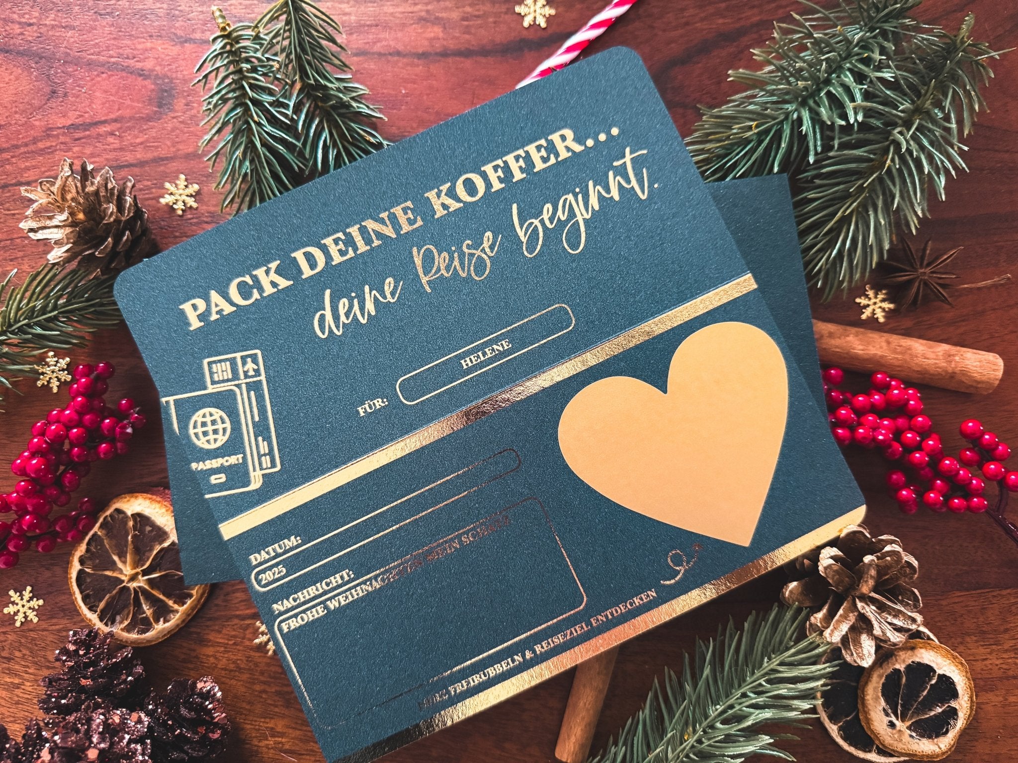 Die funkenschauer Rubbelkarte "KREATIVE WEIHNACHTSGESCHENKE | PERSONALISIERTER REISEGUTSCHEIN FROHE WEIHNACHTEN" mit Goldakzenten liegt dekorativ auf Holz, umgeben von Tannenzweigen, Zimt, Zapfen und Orangenscheiben.