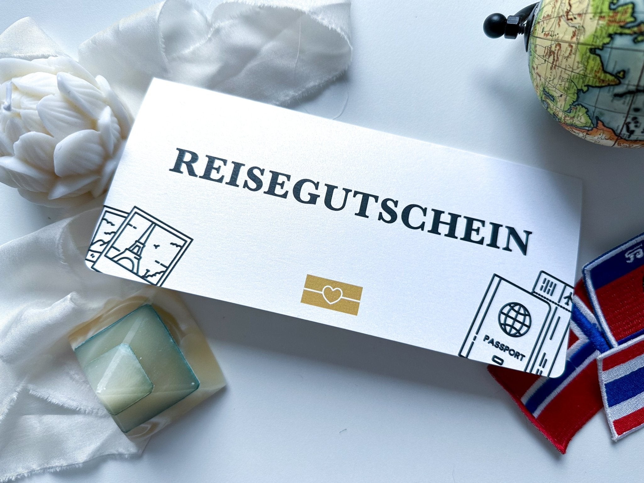 Der Funkenschauer „Reisegutschein zum Verschenken“ enthält ein Weltkartenmotiv, einen Reisepass und Wahrzeichenillustrationen. Es ist mit einem Band, einem Globus, einer weißen Blume und bunten Aufnähern verziert – was es zum perfekten personalisierten Geschenk für jeden Reiseliebhaber macht.