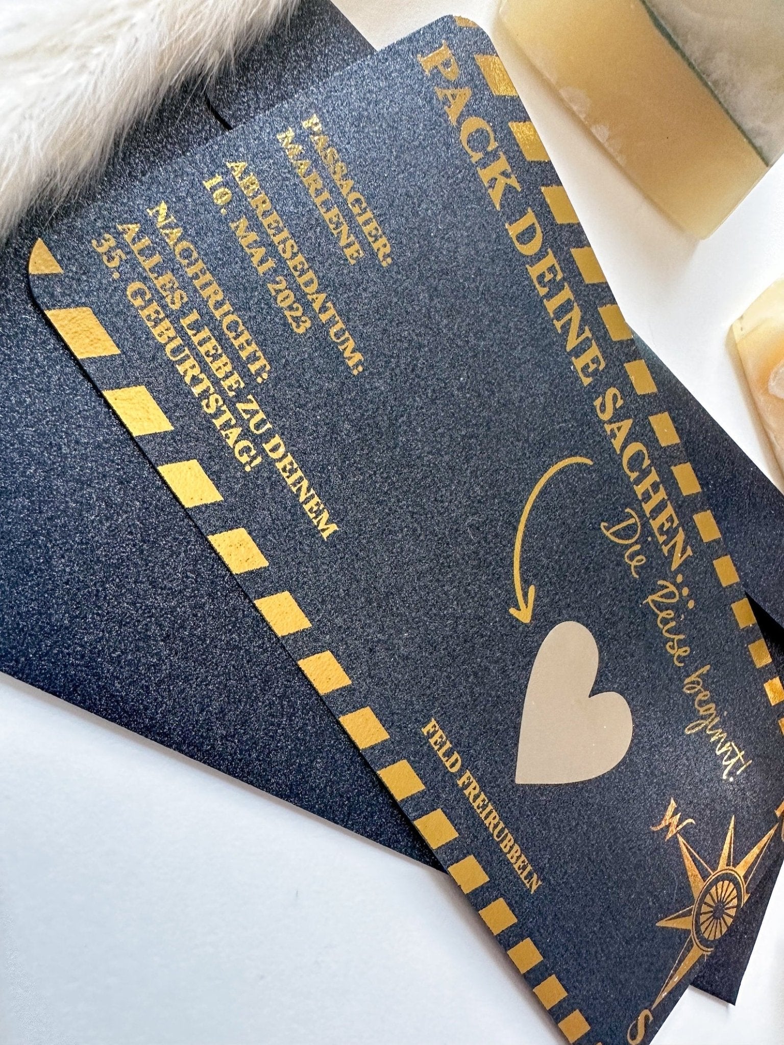 Eine Nahaufnahme von zwei funkenschauer Reisegutscheinen im Bordkarten-Design mit Goldschrift, Herzsymbol, Kompassrose und Streifenrand – personalisierbare Rubbelkarten als Geschenk für Reiseliebhaber, umgeben von Deko.