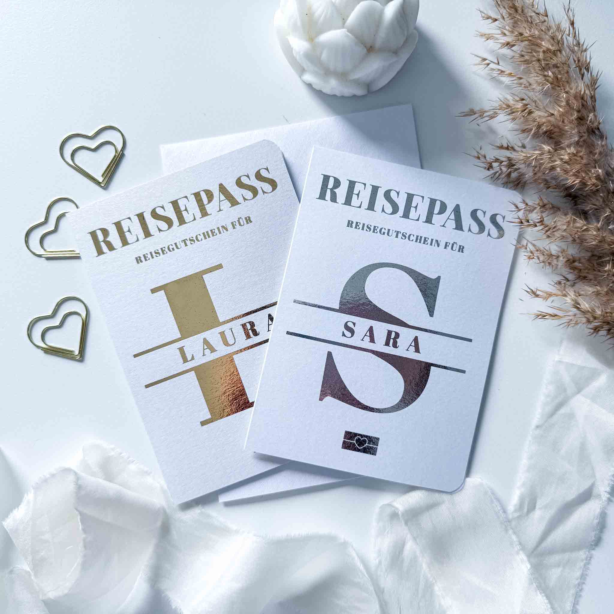 Zwei weiße "funkenschauer" Booklets, personalisierte Reisepässe als Reisegutschein mit Umschlag und Rubbelkarte für Laura und Sara, umgeben von Herzpapierklammern, Trockenblumen und Muschel - die perfekte Geschenkidee für den nächsten Urlaub!.