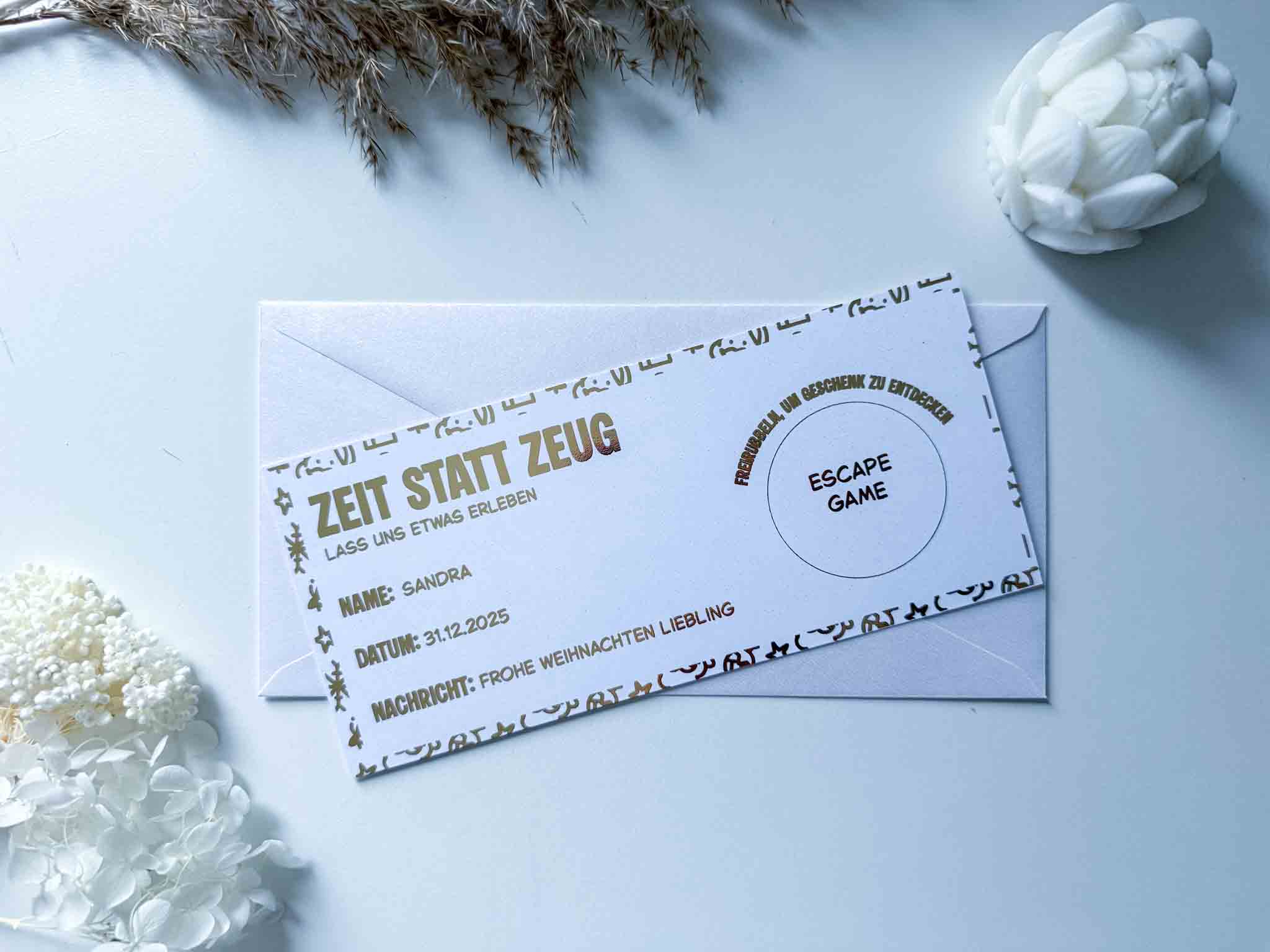 Die personalisierte Gutschein Weihnachten Zeit statt Zeug Rubbelkarte von funkenschauer liegt auf einem weißen Umschlag, umgeben von getrockneten Blumen. Felder für Name, Datum und Nachricht sind enthalten.