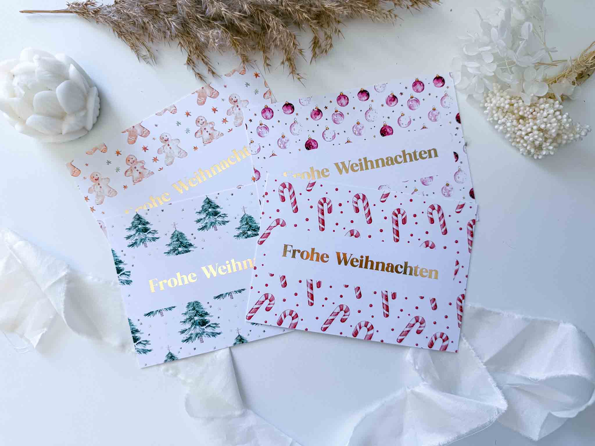 Drei festliche "Frohe Weihnachten"-Karten von funkenschauer mit Bäumen, Zuckerstangen und Ornamenten, arrangiert mit Schleifenband, Trockenblumen und einer "Weihnachten Gutschein Zeit statt Zeug"-Rubbelkarte plus handgefertigtem Umschlag.