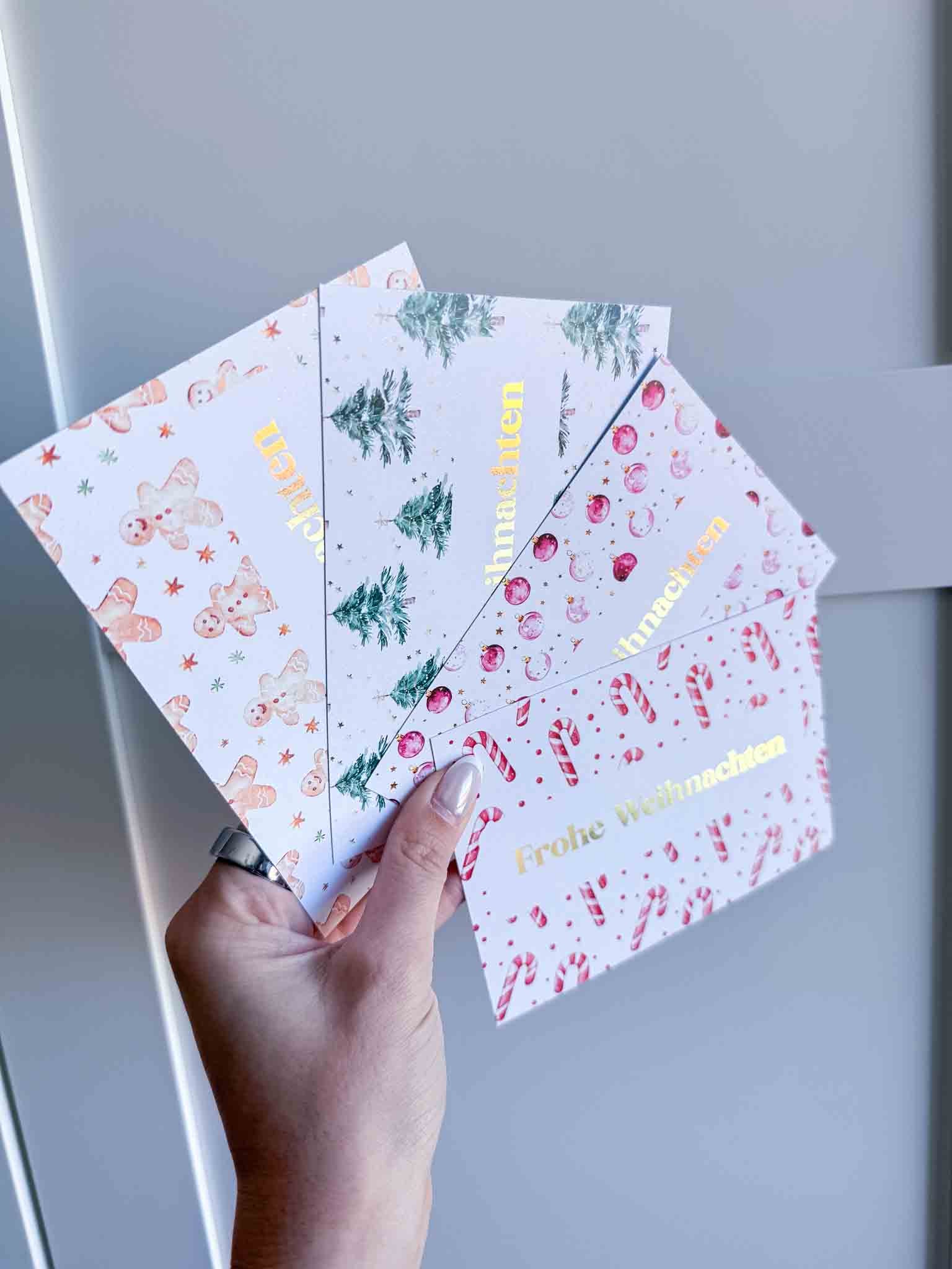 Eine Hand hält fünf festliche funkenschauer Weihnachtskarten, darunter "Weihnachten Gutschein Zeit statt Zeug" Rubbelkarten - handgefertigte Gutscheine für besondere Momente, mit Motiven wie Lebkuchenmännern, Tannenbäumen und "Frohe Weihnachten" in Gold.